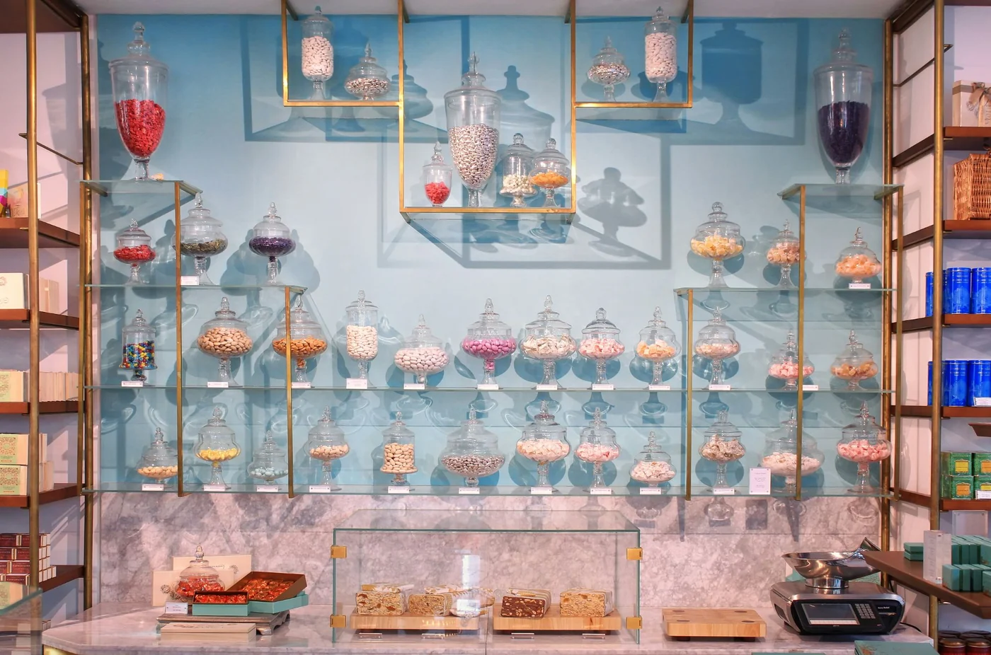 A candy shop wall of glass apothecary jars on brass shelves against pale blue